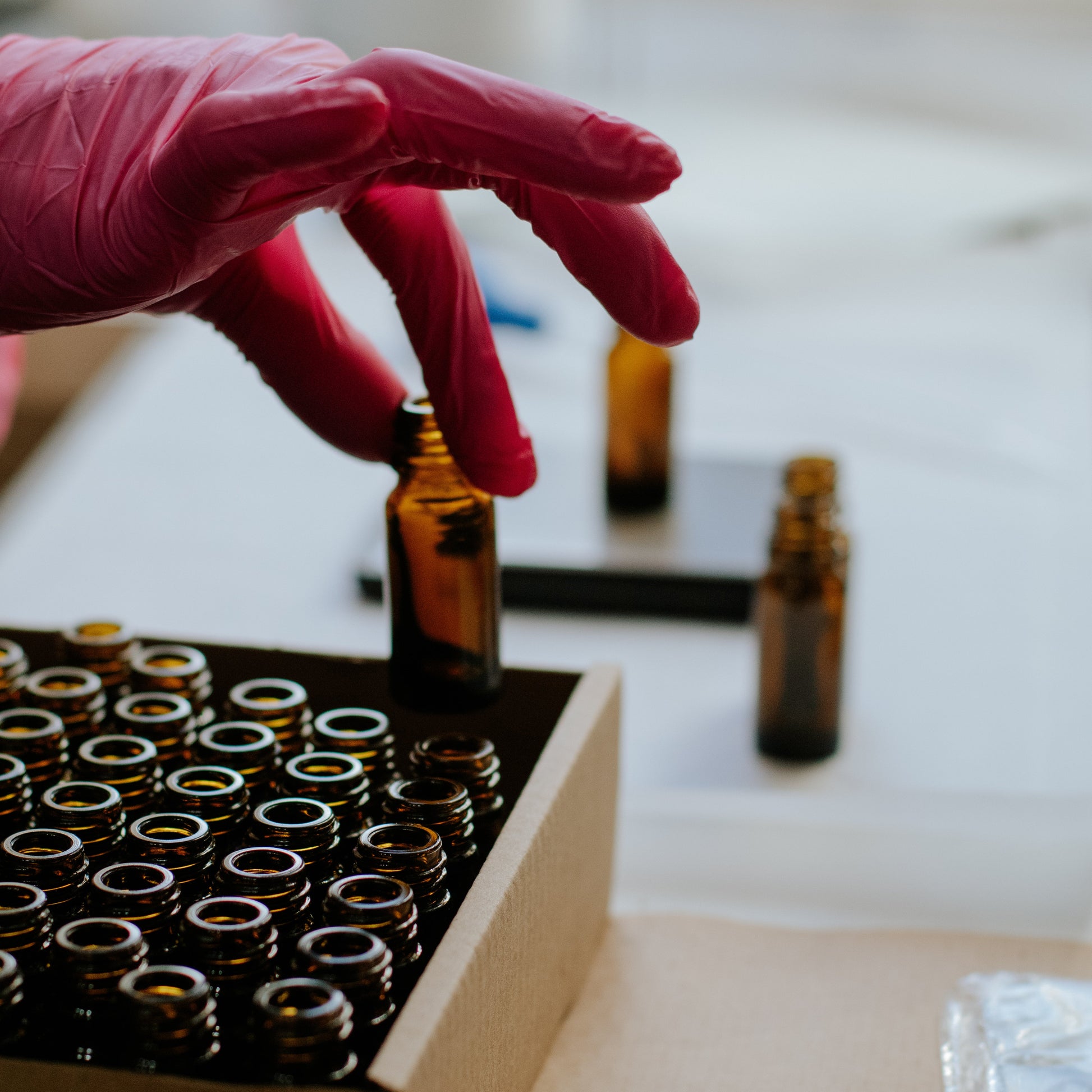 Hand in a pink glove handling small brown bottles on a white surface.